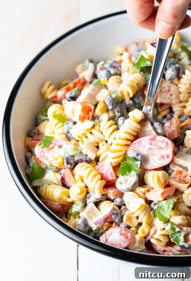 Fiesta Pasta Salad 11 A hand holding a spoon and scooping creamy southwest pasta salad out of the salad bowl, showing its texture and ingredients.