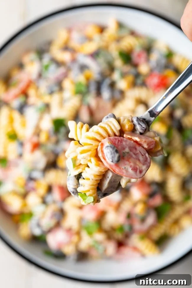 Fiesta Pasta Salad 4 A hand holding a spoon with a scoop of creamy Southwest pasta salad over the serving bowl.