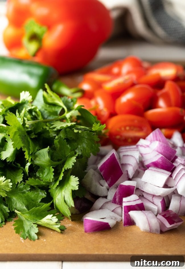 Fiesta Pasta Salad 5 Chopped cilantro, red onion, grape tomatoes, and red bell pepper on a cutting board, ready for the salad.