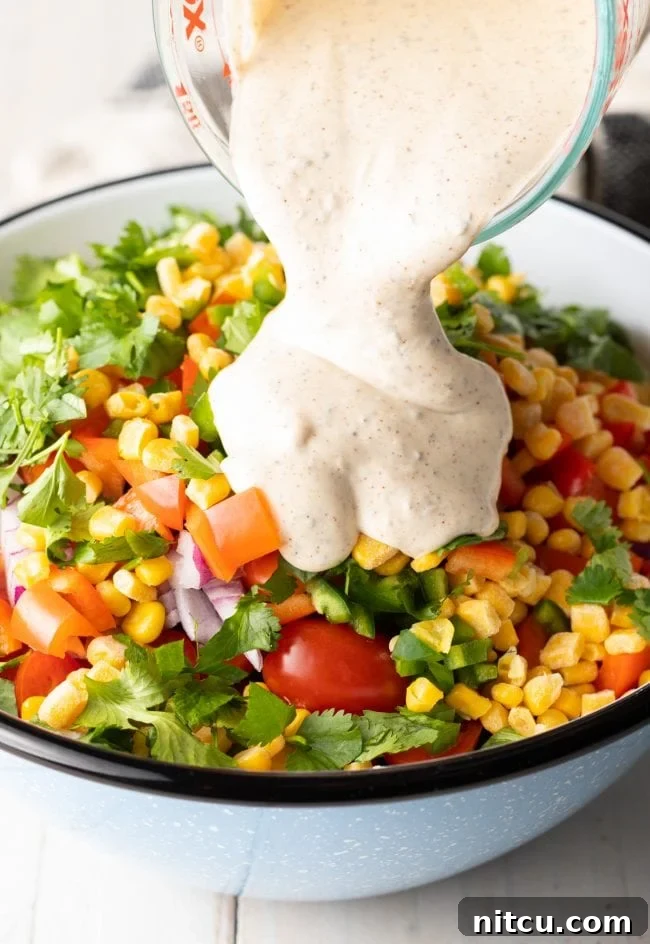 Fiesta Pasta Salad 8 Creamy ranch dressing being poured over the salad ingredients in a large bowl.