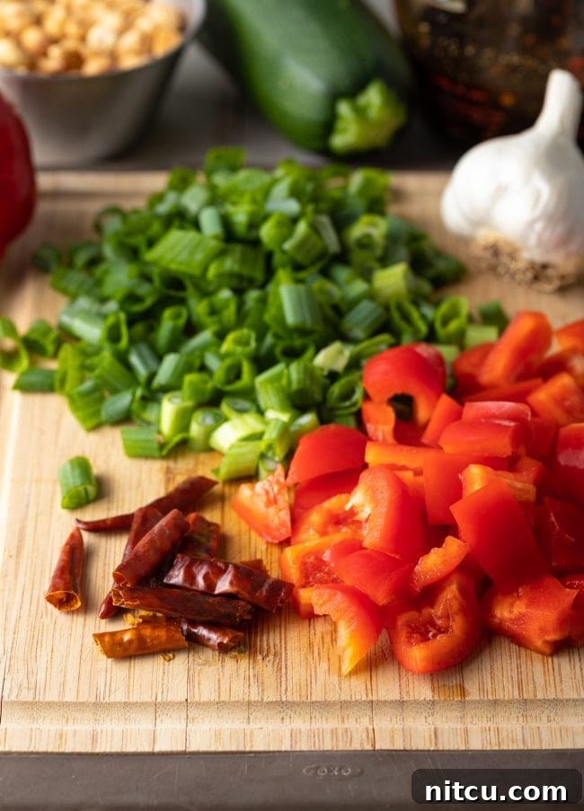 Sichuan Kung Pao Chicken 5 Diced bell peppers, scallions, red chiles and a bulb of garlic on a cutting board.