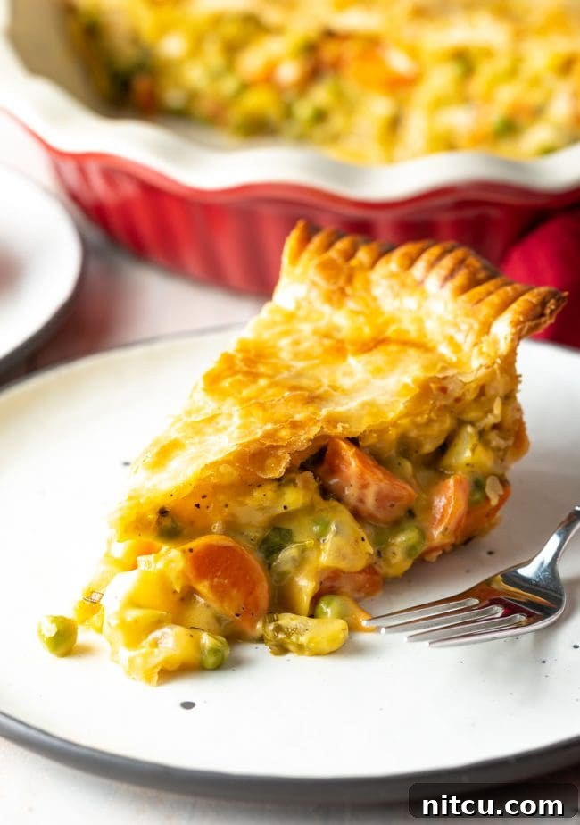 A close-up shot of the vegetarian pot pie filling, showing a medley of carrots, peas, celery, and creamy gravy beneath a golden crust.