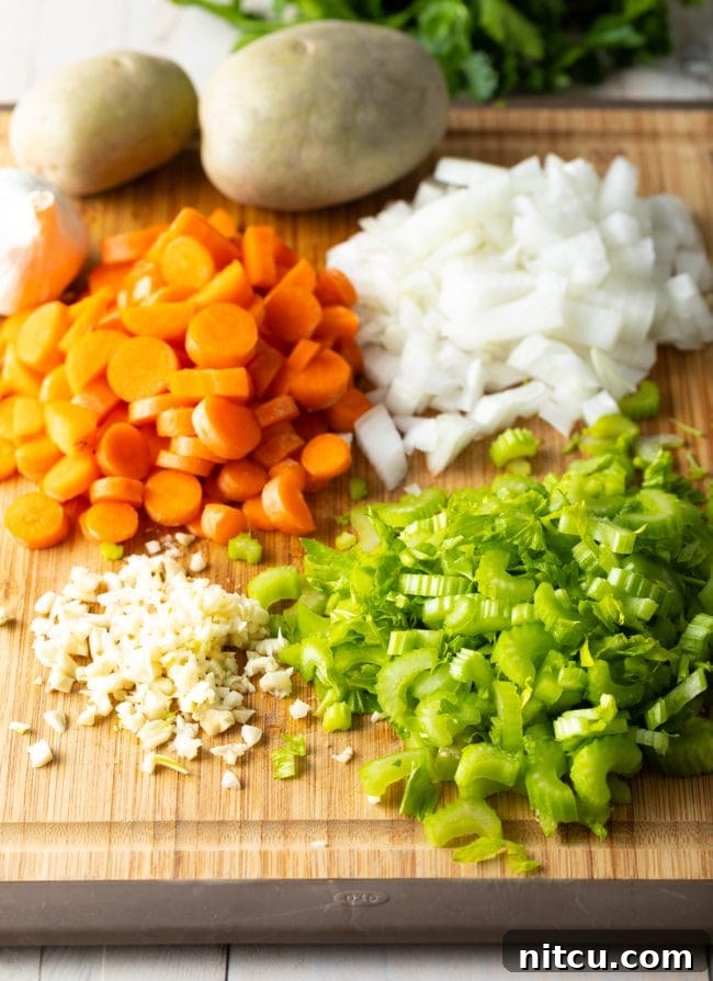 Diced carrots, onions, celery, and minced garlic neatly arranged on a wooden cutting board, ready for cooking.