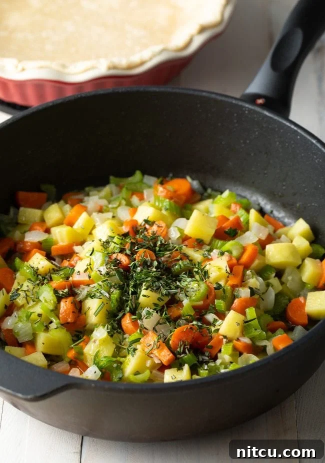Sautéed vegetables, including carrots, potatoes, and celery, mixed with fragrant seasonings in a large skillet, creating a rich aroma.