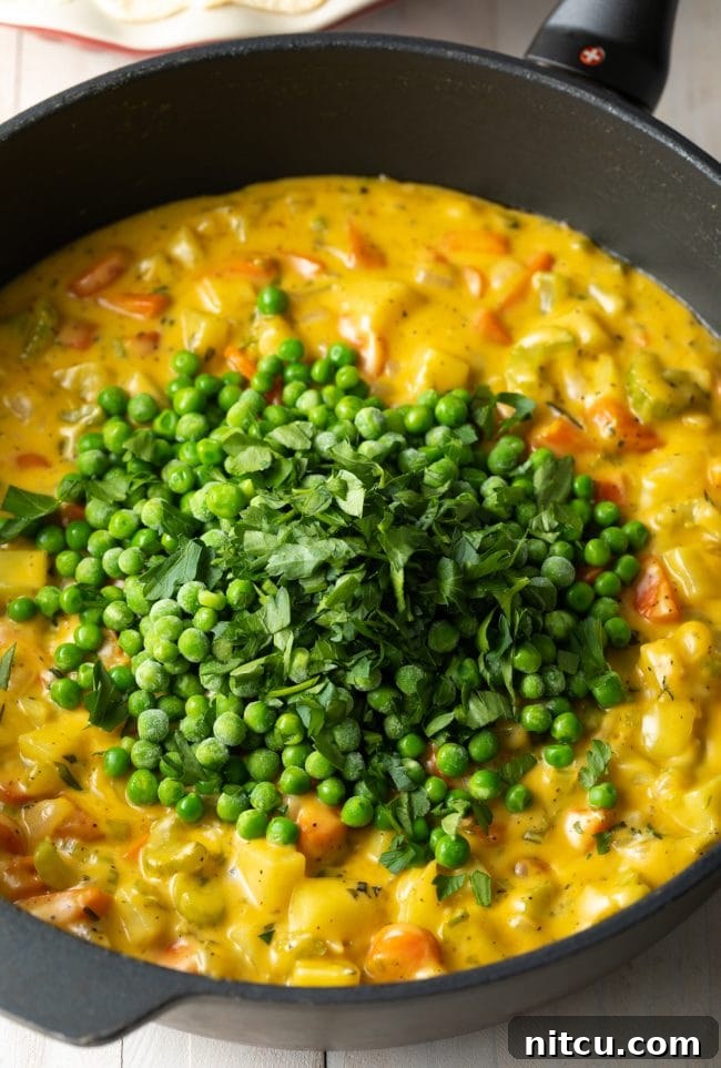 A creamy vegetable pot pie filling simmering in a skillet, featuring sautéed vegetables, heavy cream, frozen peas, and fresh cilantro, creating a vibrant and rich mixture.