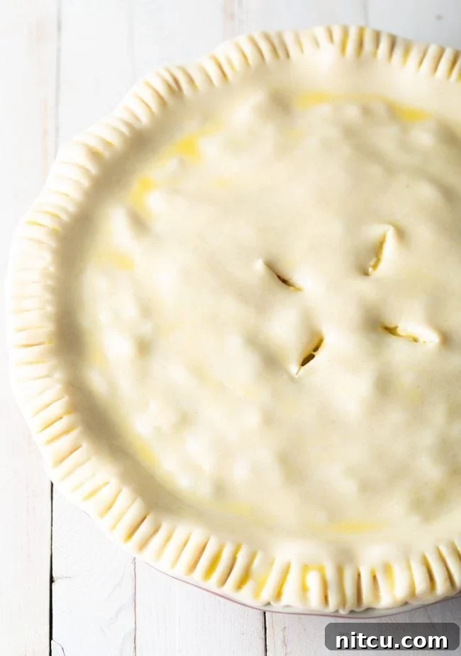 An uncooked pie crust in a pie dish, brushed with a golden egg wash, ready for baking.