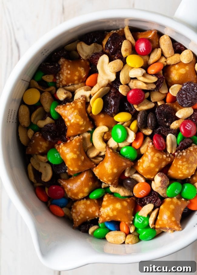Wholesome DIY Trail Mix 3 Sweet and salty indulgent trail mix recipe in a white bowl, featuring pretzels, candies, and dried fruit.