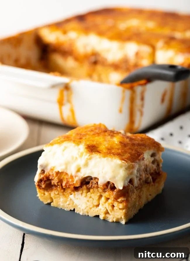 Hearty Greek Pastitsio Casserole 2 Greek pastitsio square with meat sauce and bechamel, on a gray plate.