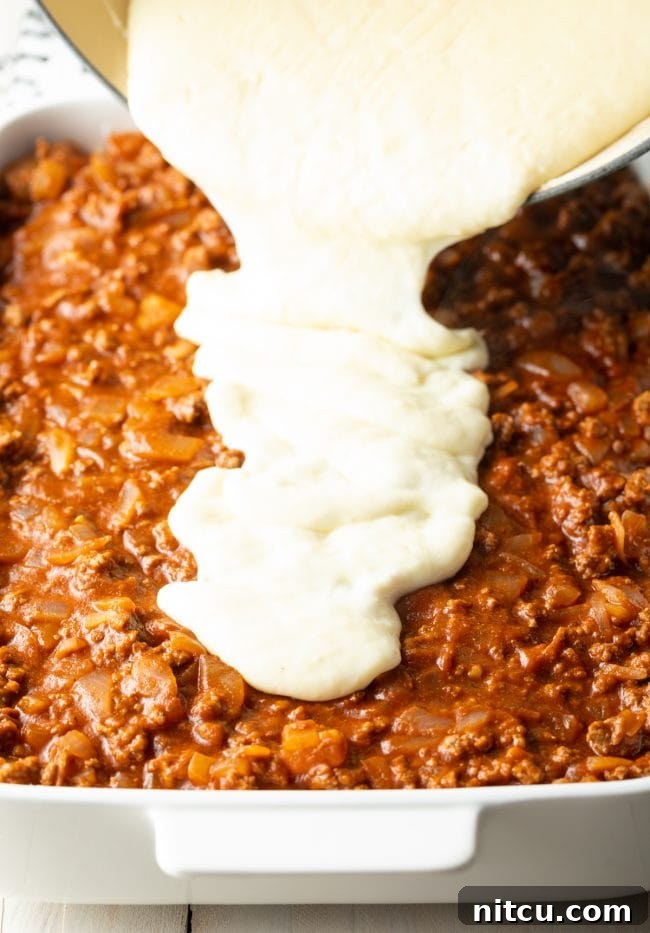 Hearty Greek Pastitsio Casserole 11 Pouring creamy bechamel sauce over the meat sauce.