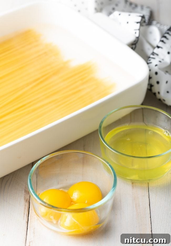 Hearty Greek Pastitsio Casserole 5 Bucatini pasta in a white baking dish, glass bowl with egg yolks and separate glass bowl with egg whites.