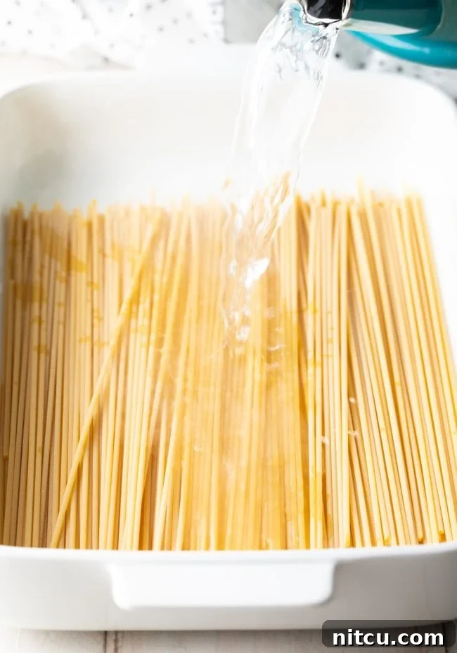 Hearty Greek Pastitsio Casserole 6 Pouring hot water over bucatini pasta in a white baking dish.