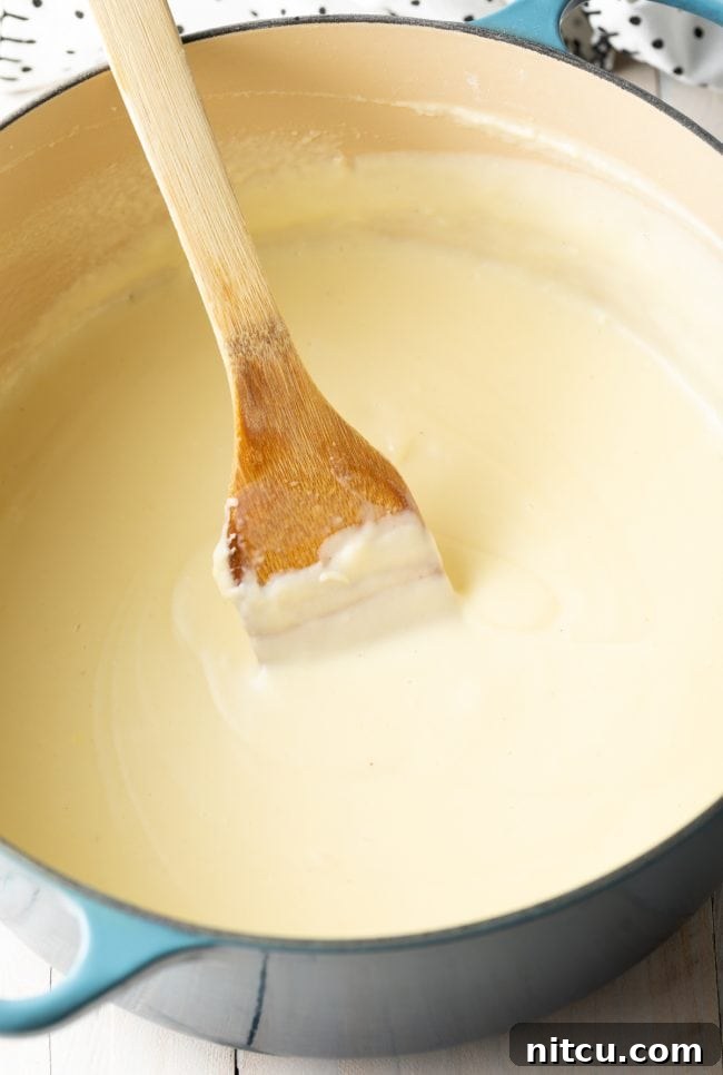 Hearty Greek Pastitsio Casserole 7 Stirring creamy bechamel sauce with a wooden spatula.