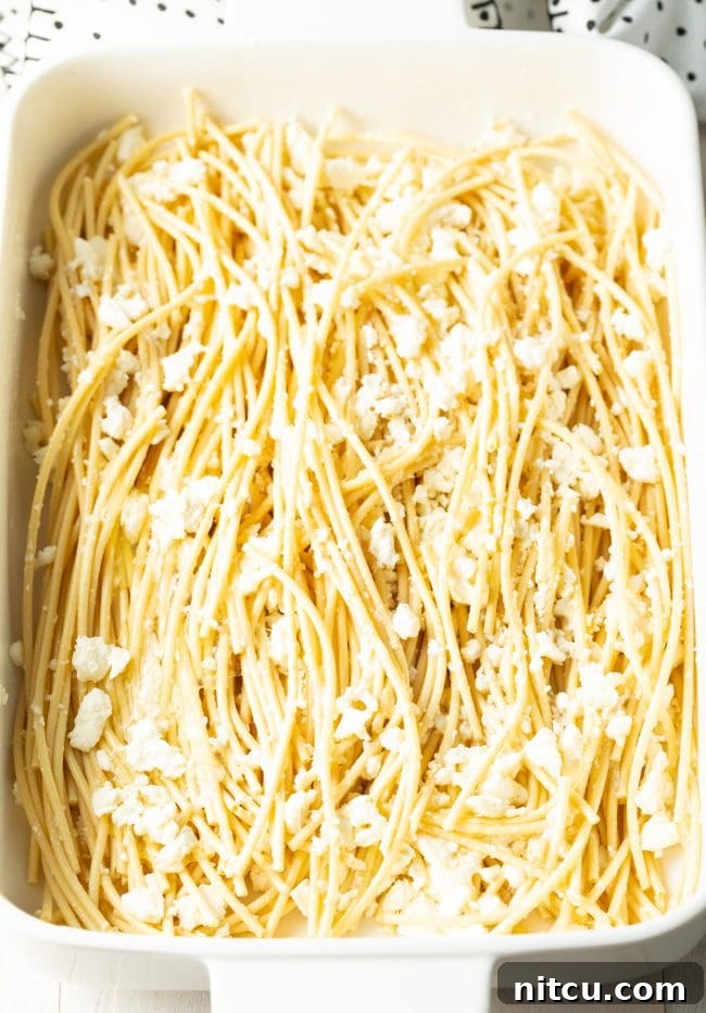 Hearty Greek Pastitsio Casserole 8 Soaked bucatini in a white baking dish, topped with crumbled Greek feta cheese.