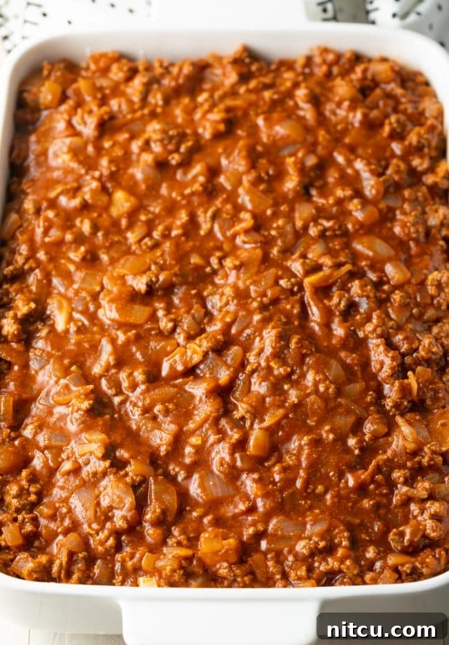 Hearty Greek Pastitsio Casserole 10 Zesty tomato meat sauce poured on top of pasta in a white baking dish.