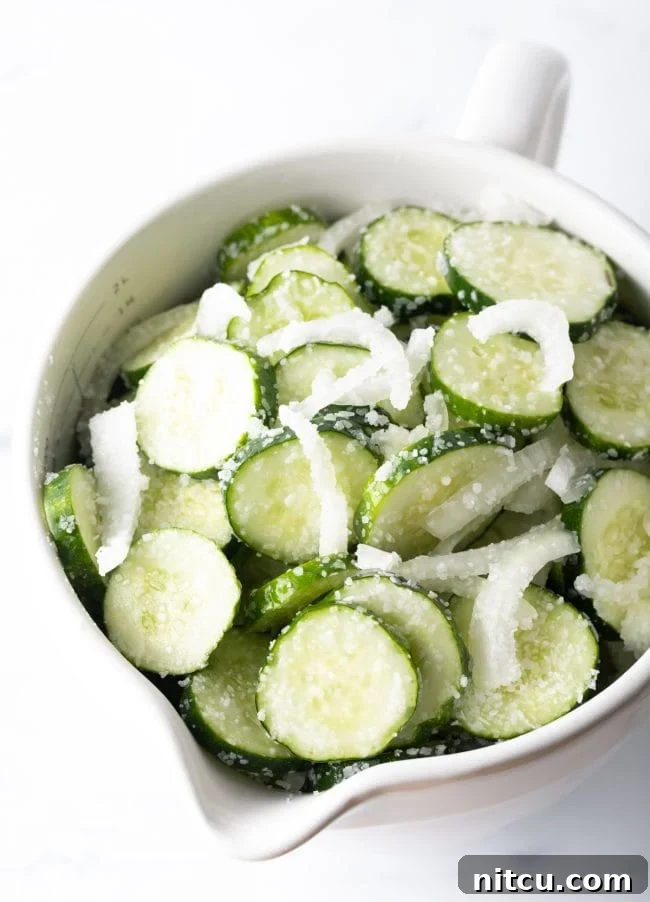 Effortless Homemade Bread & Butter Pickles 7 White bowl with sliced cucumbers and white onion.