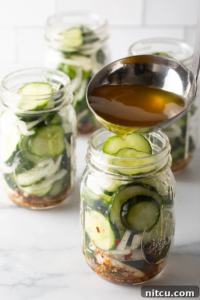 Effortless Homemade Bread & Butter Pickles 10 Using a metal ladle to pour pickling liquid into glass jars with sliced cucumbers and onions.