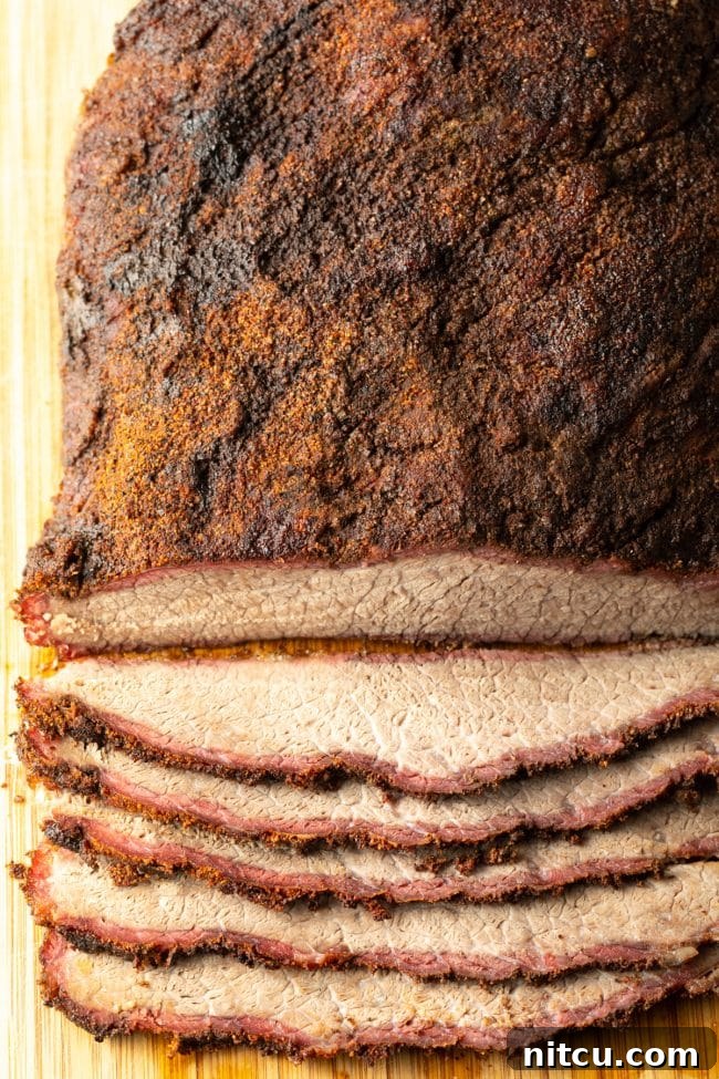 Ultimate Dry-Brined Smoked Brisket 2 Perfectly smoked beef brisket resting on a wooden cutting board, with several slices already carved.