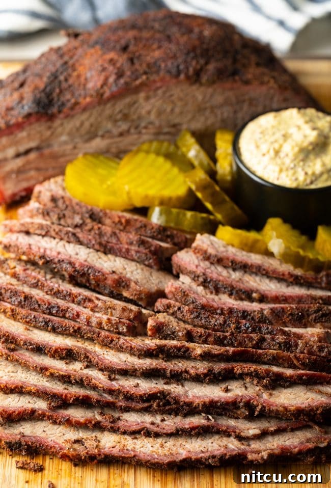 Ultimate Dry-Brined Smoked Brisket 16 Smoked beef brisket perfectly sliced on a wooden cutting board, accompanied by pickles and mustard for serving.