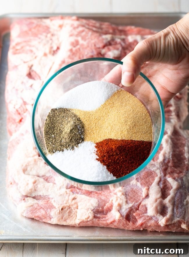 Ultimate Dry-Brined Smoked Brisket 6 Dry brisket brine spice rub being applied by hand to a raw beef brisket on a baking sheet.