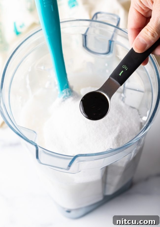 Creamy Dairy-Free Coconut Ice Cream 6 adding vanilla to the blender with coconut milk in it.