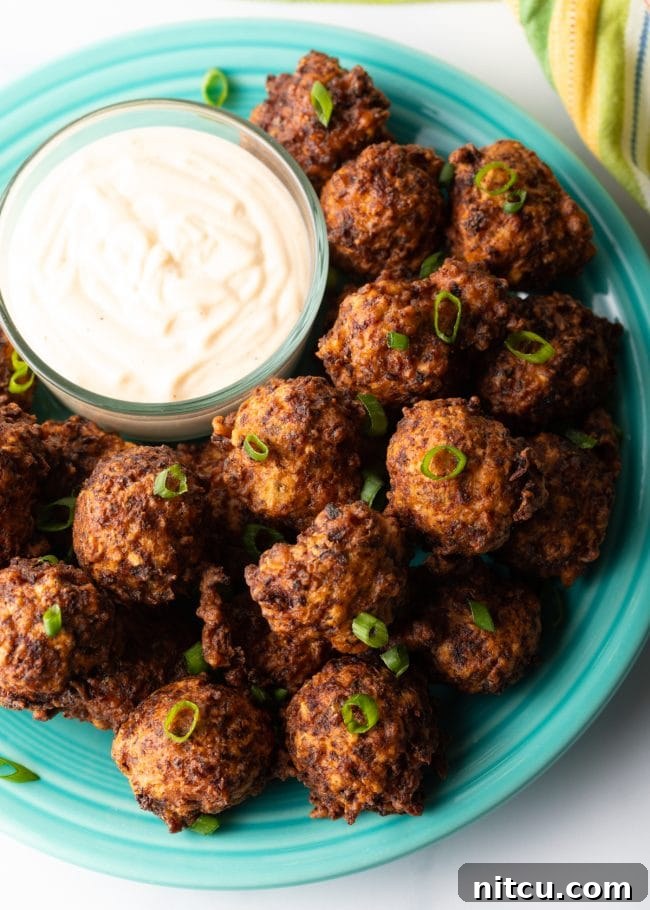 A plate of freshly fried seafood balls, Bahamian conch fritters, garnished with fresh herbs and served with a ramekin of remoulade sauce.