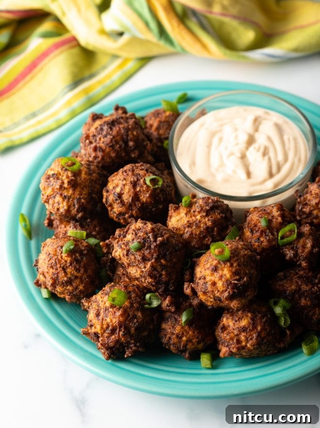 A side view of a plate laden with golden-brown conch fritters, accompanied by a small bowl of creamy dipping sauce, ready for serving.