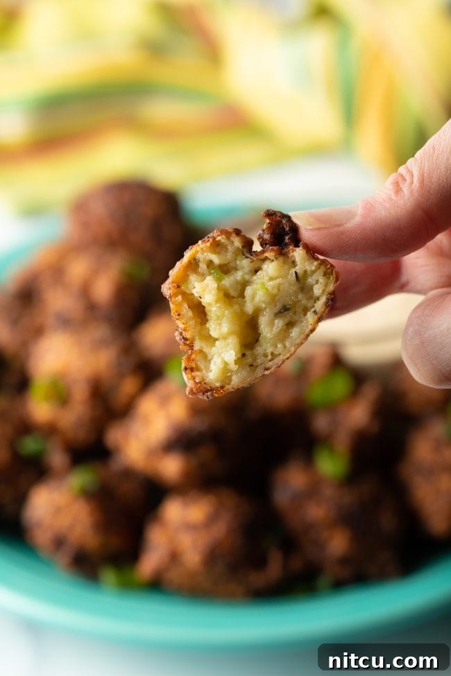 A close-up view of a freshly fried Bahamian conch fritter, showing its moist, flavorful interior and perfectly golden, crisp exterior, inviting a delicious bite.