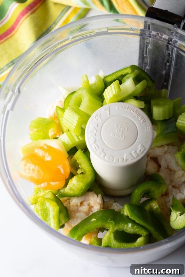 Chopped celery and bell peppers being added to the food processor with the pre-chopped conch meat, for further processing into a fine mixture for fritters.