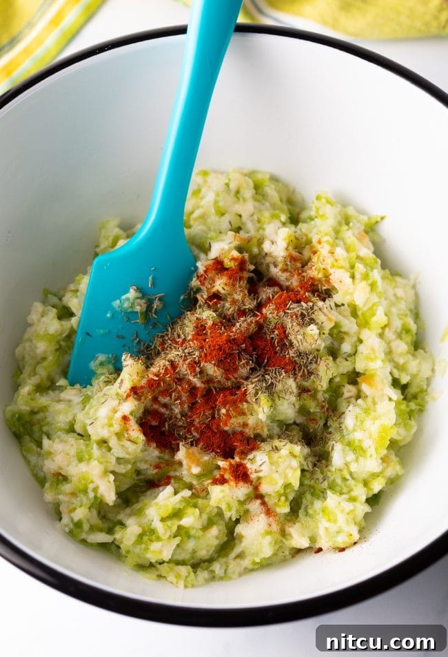 Various spices including paprika, thyme, salt, and pepper being added to the conch and vegetable mixture in a mixing bowl for the conch fritters recipe.