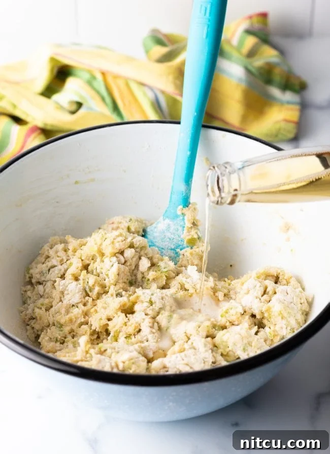 A stream of light beer being poured into the conch fritter batter in a mixing bowl, to achieve the desired consistency.
