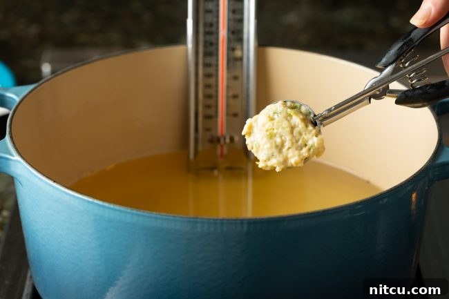 A scoop of conch fritter batter being carefully dropped into hot frying oil, creating a sizzle and starting the cooking process.