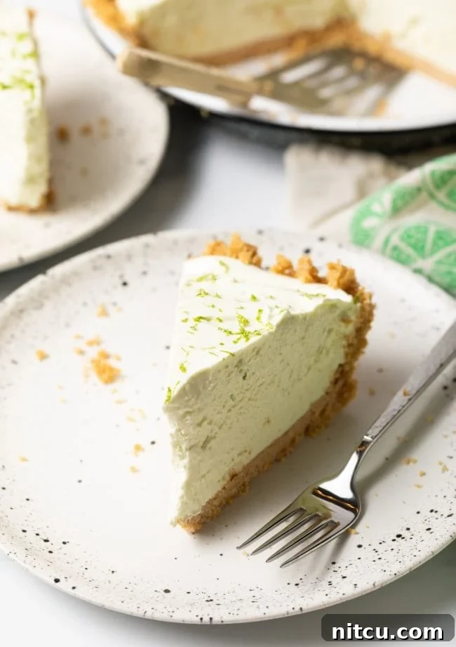 Effortless Key Lime Pie 2 A vibrant slice of no-bake key lime pie presented on a pristine white plate, accompanied by a fork, ready to be enjoyed.