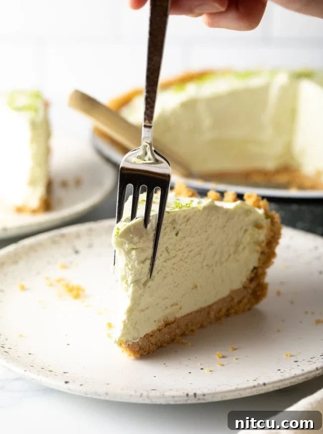 Effortless Key Lime Pie 13 A delicious slice of key lime pie on a plate with a fork, showing a bite already taken, highlighting the creamy texture and inviting taste.