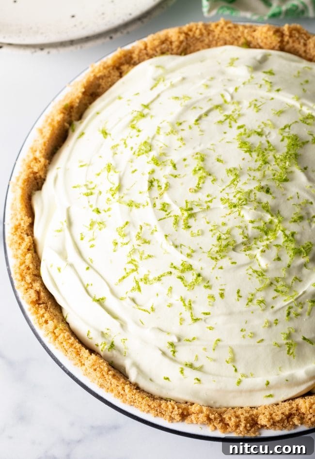 Effortless Key Lime Pie 3 A perfectly prepared full no-bake key lime icebox pie, featuring a golden graham cracker crust and generously sprinkled with fresh lime zest on top, waiting to be sliced.