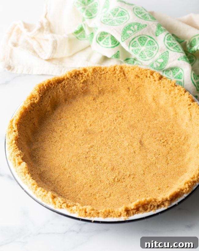 Effortless Key Lime Pie 7 A neatly pressed graham cracker crust mixture forming an even layer in a pie plate, prepared and chilled, awaiting its delicious filling.