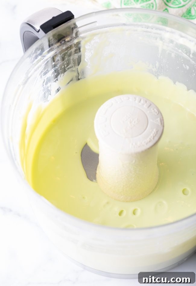 Effortless Key Lime Pie 8 A bright green key lime pie filling mixture, smooth and creamy, swirling inside a food processor bowl, ready for the next step.