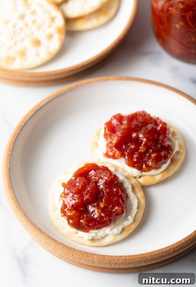 An overhead view of a rustic plate featuring two crackers, elegantly topped with creamy cheese and a dollop of this exquisite tomato jam recipe.
