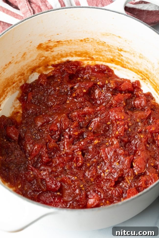Homemade tomato jam gently simmering in a pot, its vibrant color and thickening consistency hinting at its rich flavor.