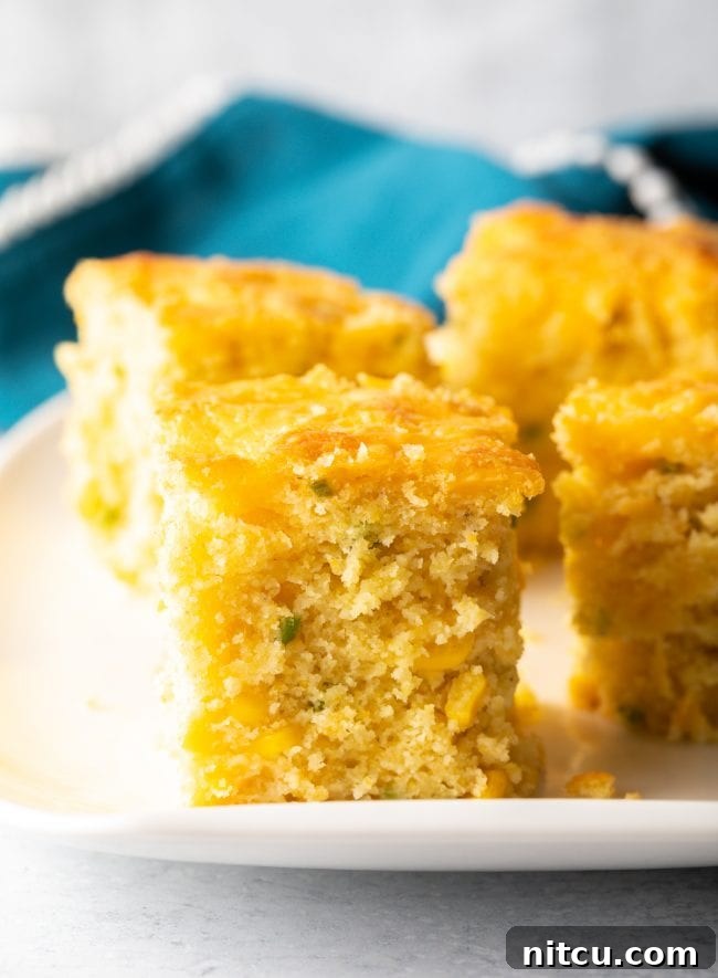 Zesty Jalapeno Cheddar Cornbread 12 Perfectly cut squares of homemade cheesy cornbread with visible chopped peppers, ready to be served.
