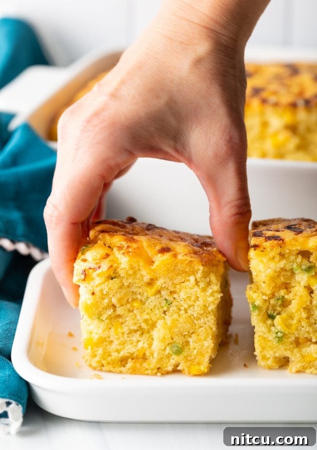 Zesty Jalapeno Cheddar Cornbread 4 A hand reaching for a piece of this delectable jalapeno cheddar cornbread, highlighting its golden crust and inviting texture.