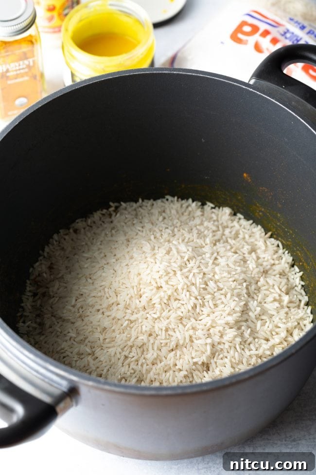 White rice added to the sautéed vegetables in a pot, ready to be coated with butter.