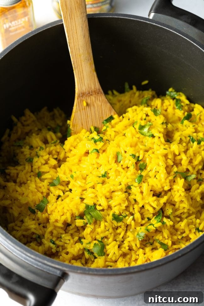 A wooden spoon gently mixes the yellow rice with fresh cilantro, preparing it for serving.