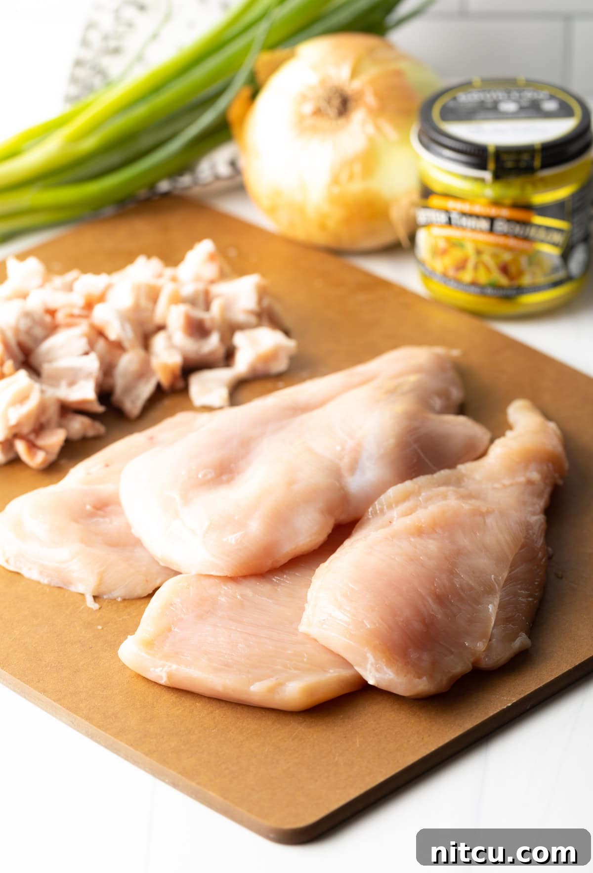Braised Chicken Delight 4 Ingredients for Smothered Chicken laid out on a cutting board, including raw chicken breasts, bacon, onion, and spices.
