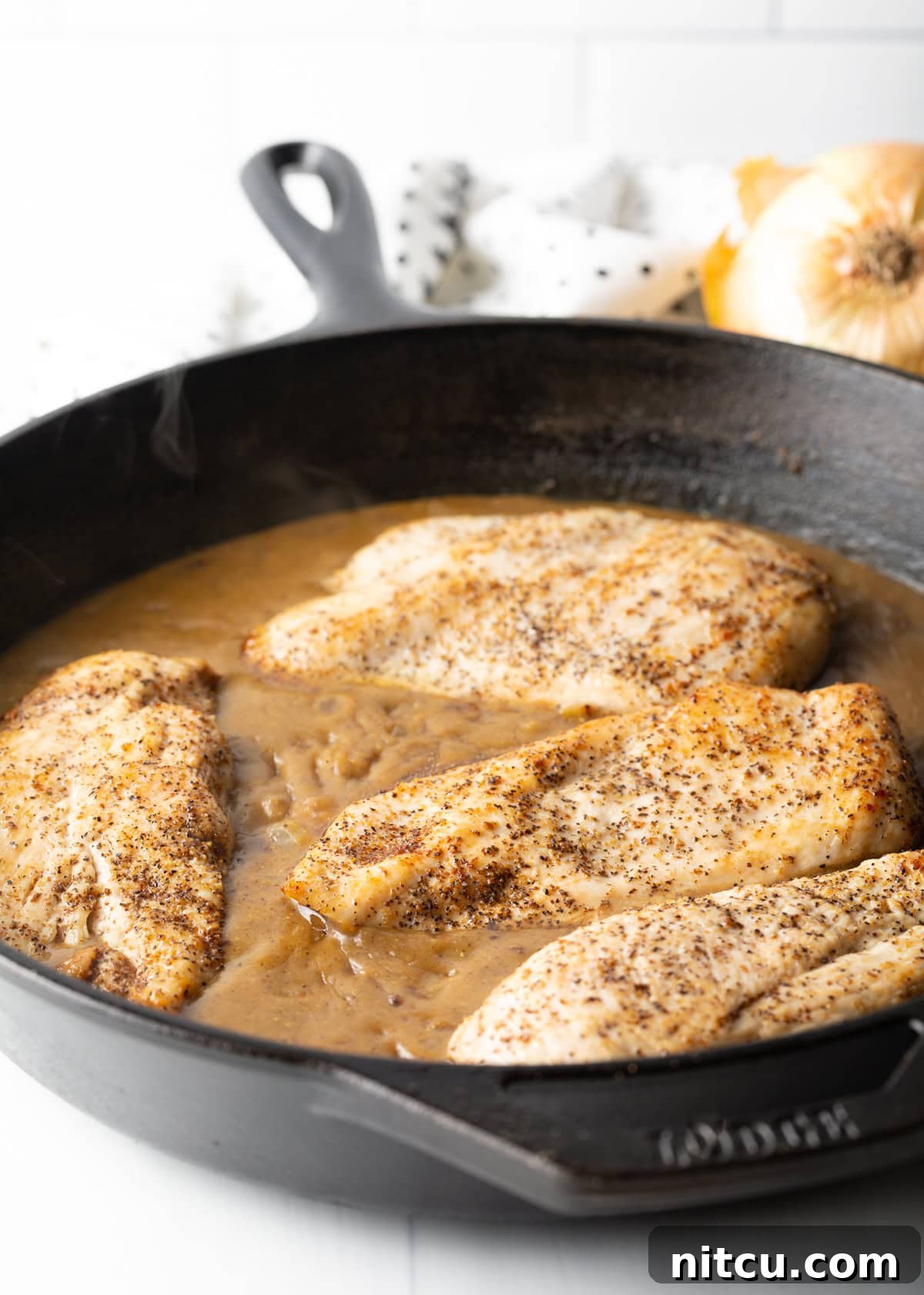Braised Chicken Delight 8 Tender chicken breasts coated in a rich brown gravy, simmering in a heavy cast iron skillet.