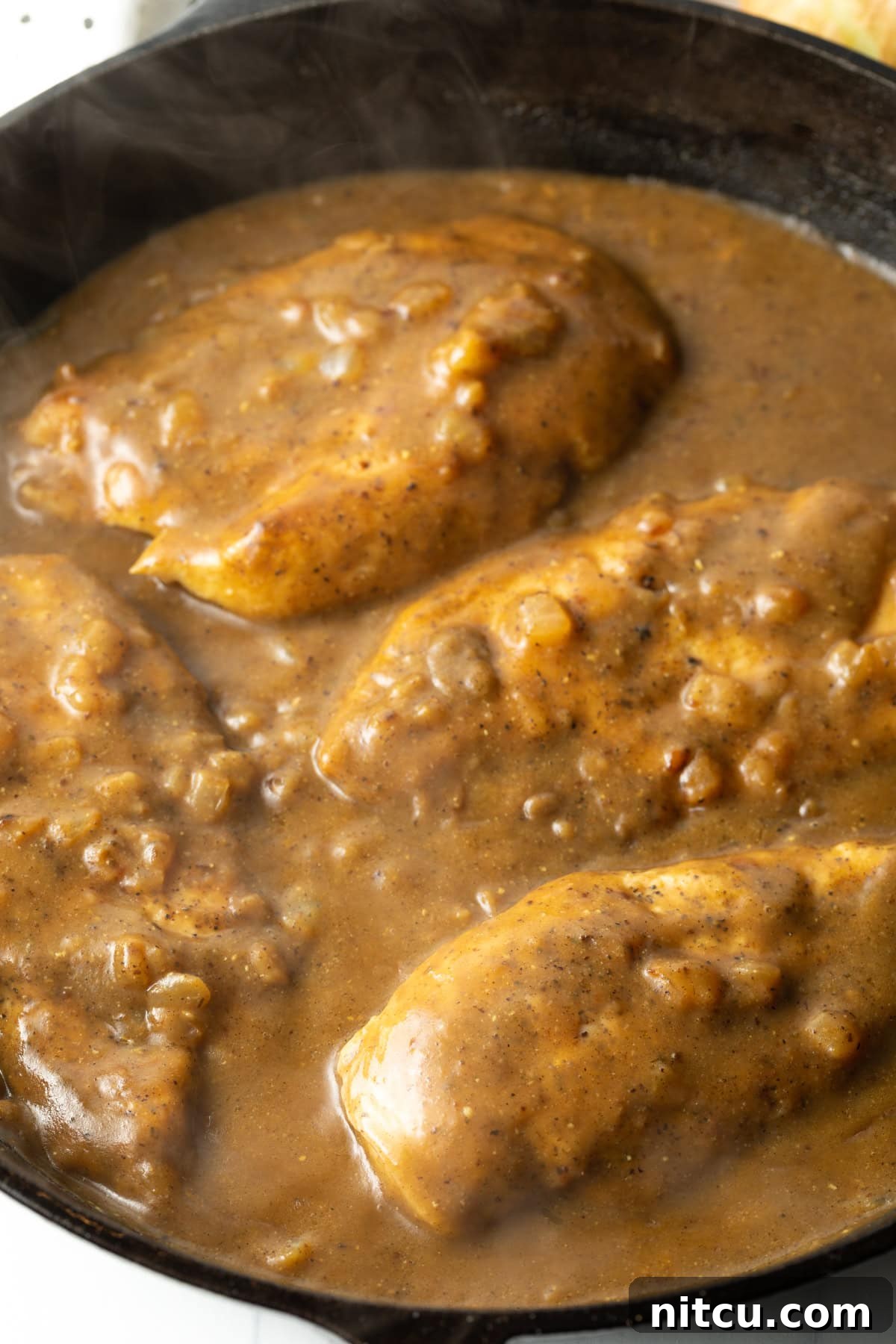 Braised Chicken Delight 9 Overhead view of boneless, skinless chicken smothered in rich gravy with melted cheese, bacon, and scallions in a cast iron skillet.