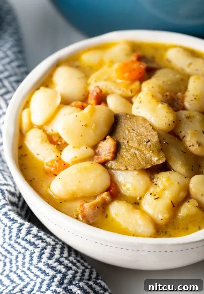 Close-up view of a serving of classic Southern butter beans with crispy bacon pieces and finely diced vegetables, showcasing their tender, creamy texture.