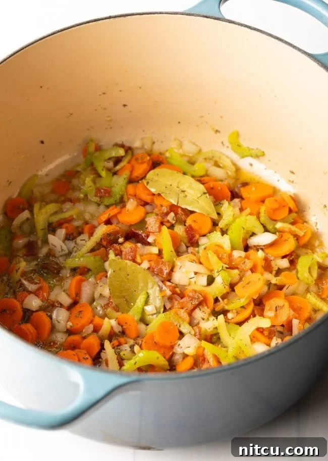 The aromatic vegetable trinity of diced celery, sliced carrots, and chopped onions gently cooking in a large, heavy-bottomed pot, releasing their fragrances.