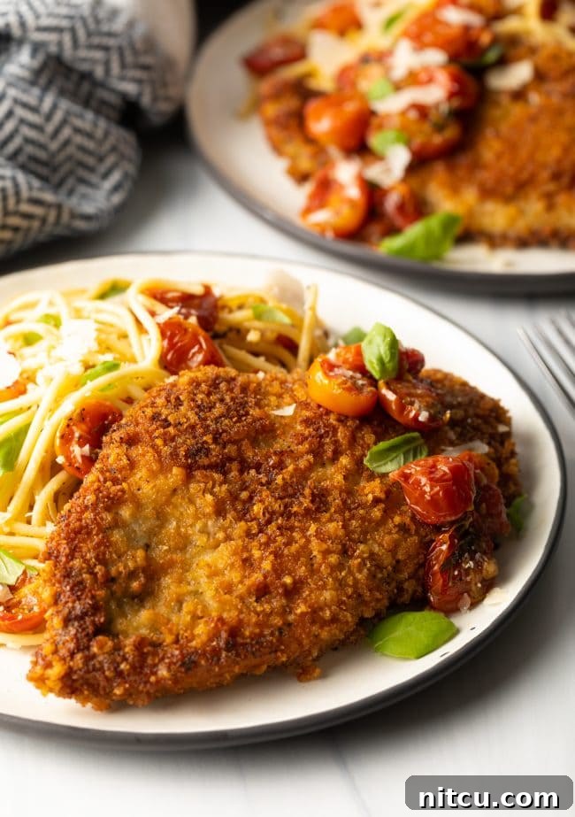 Crispy Italian Chicken Cutlets 2 side view breaded fried Italian chicken cutlets on a plate with pasta and tomatoes and micro basil