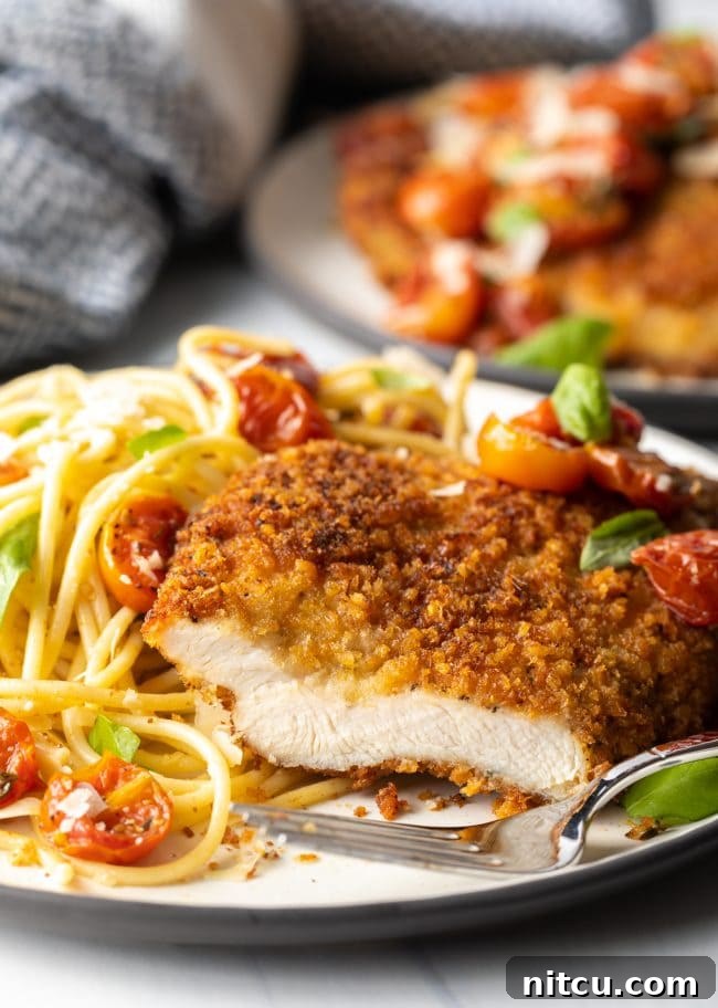 Crispy Italian Chicken Cutlets 4 cut breast showing meat inside, on a plate with fork and pasta