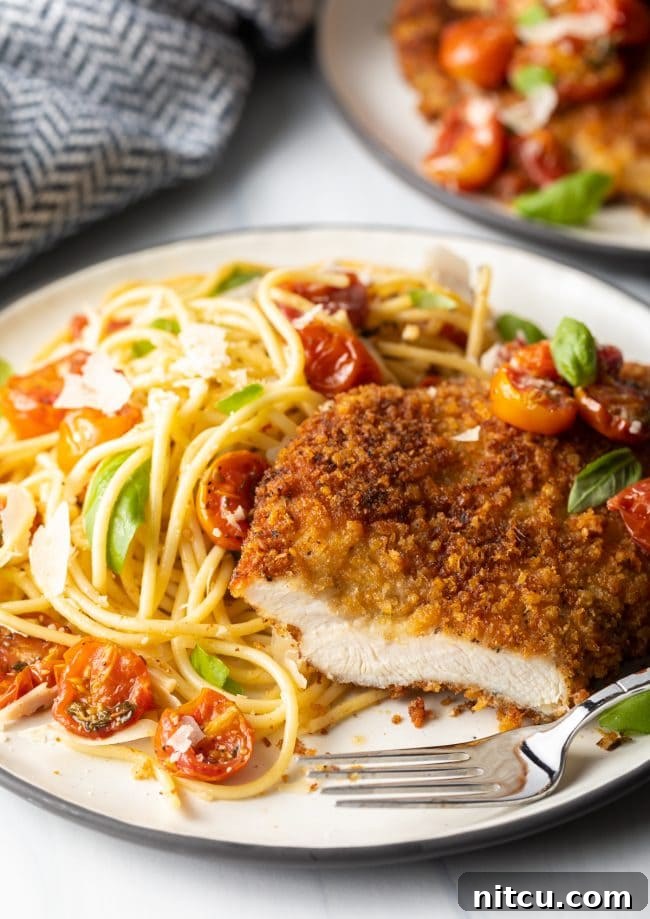 Crispy Italian Chicken Cutlets 10 final shot showing Italian chicken cutlet cut into with a fork on a plate, spaghetti and cherry tomato sauce on the side